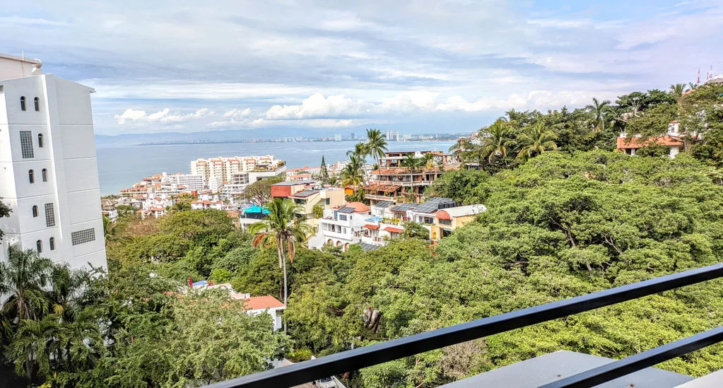 Daylight view from an Amapas condo balcony over lush trees, low-rise buildings, and Banderas Bay